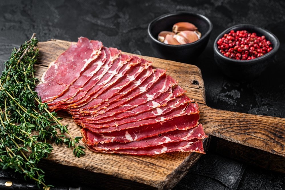 Fatias de pastrami gourmet fresco em tábua de madeira com tomilho e especiarias, ideal para receitas