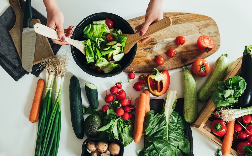 Pessoa preparando salada com variedade de legumes frescos — refeição leve e colorida