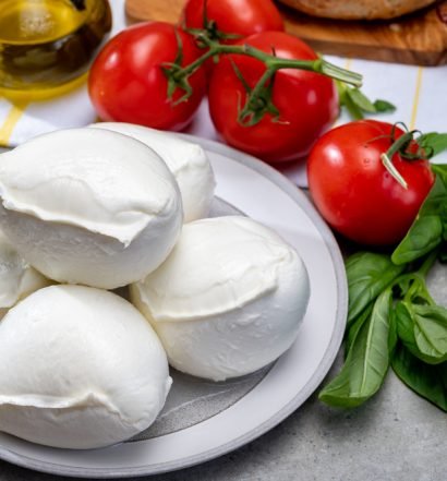 Porções de queijo de búfala sobre tábua de madeira com tomates-cereja e manjericão