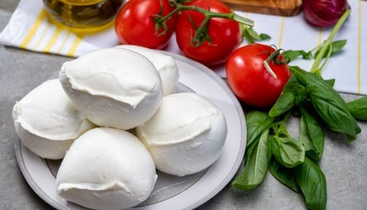 Porções de queijo de búfala sobre tábua de madeira com tomates-cereja e manjericão