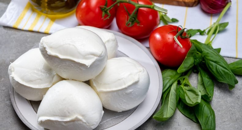 Porções de queijo de búfala sobre tábua de madeira com tomates-cereja e manjericão