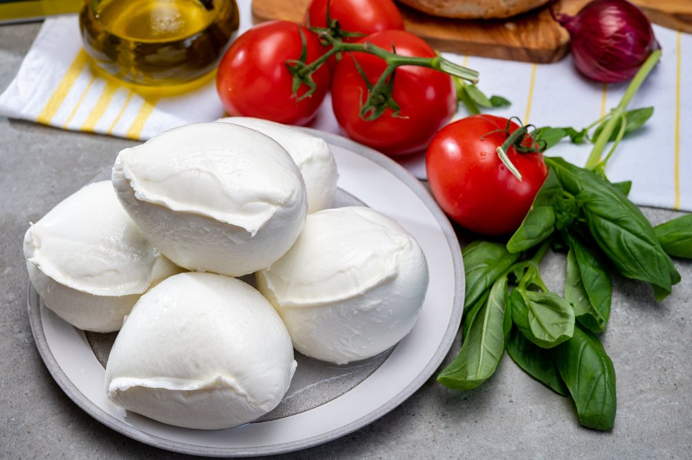 Porções de queijo de búfala sobre tábua de madeira com tomates-cereja e manjericão