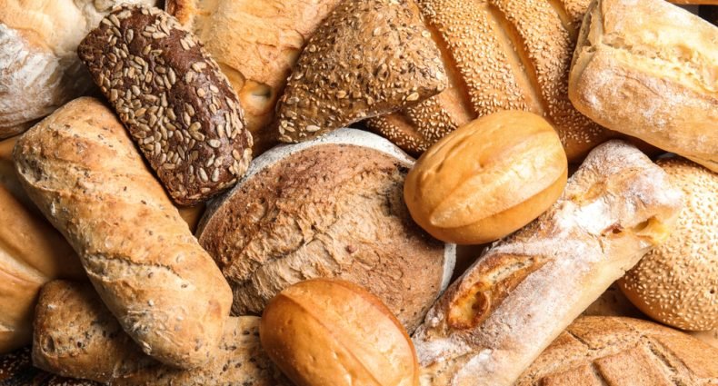Variedade de pães artesanais frescos incluindo pão integral, baguete, pão de centeio e pão com sementes para celebrar o Dia Mundial do Pão