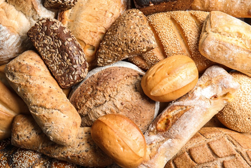 Variedade de pães artesanais frescos incluindo pão integral, baguete, pão de centeio e pão com sementes para celebrar o Dia Mundial do Pão