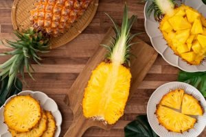 Abacaxi fresco inteiro e em pedaços sobre tábua de madeira, fruta tropical com bromelina para melhora da digestão e redução de inflamação