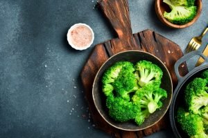 Tigela com brócolis cozido no vapor sobre tábua de madeira, vegetal rico em fibras que ajuda a baixar triglicerídeos