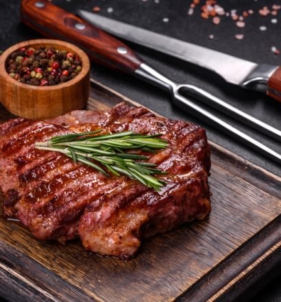 Carne vermelha grelhada com rosmaninho, tomate fresco e pimenta do reino em apresentação gourmet em tábua de madeira, com temperos em especiaria