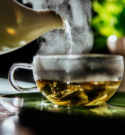 Chá quente sendo despejado em xícara de vidro, representando infusão diurética para desinchar.