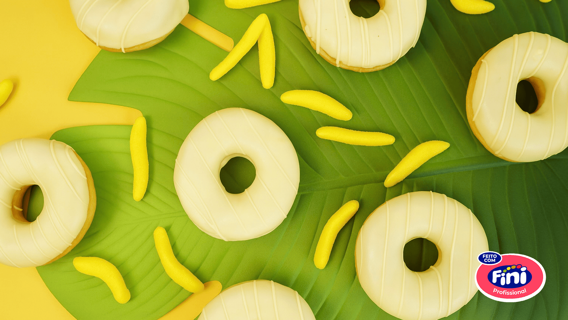 Donuts brancos tradicionais com glacê, decorados com balas Fini de banana amarela em um fundo verde tropical, representando o novo sabor Fini da padaria Pão de Açúcar.