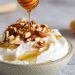 Iogurte grego cremoso com granola de nozes, mel derramado e waffle em tigela branca, alimento probiótico para melhorar a digestão