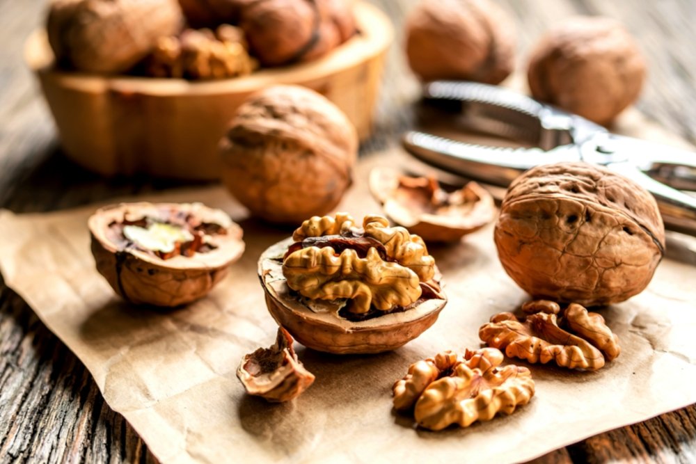 Nozes com casca e sem casca sobre papel pardo, com quebra-nozes ao fundo; gorduras boas que ajudam a reduzir triglicerídeos