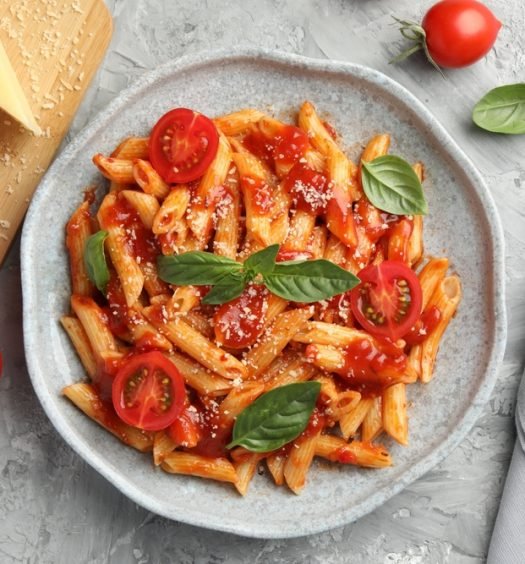 Prato de penne ao molho de tomate fresco com manjericão, tomates cereja e queijo ralado em prato cinza - receita vegetariana fácil para iniciantes