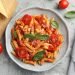 Prato de penne ao molho de tomate fresco com manjericão, tomates cereja e queijo ralado em prato cinza - receita vegetariana fácil para iniciantes