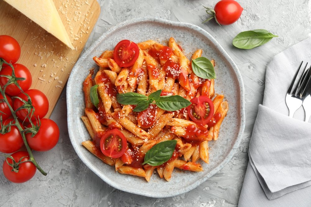 Prato de penne ao molho de tomate fresco com manjericão, tomates cereja e queijo ralado em prato cinza - receita vegetariana fácil para iniciantes