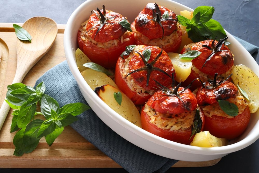 Pimentões recheados vermelhos assados em prato branco com batatas, alho e manjericão fresco