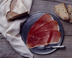 Lâminas de Jambon de Bayonne dispostas em prato metálico com pão rústico ao fundo, típico presunto francês.