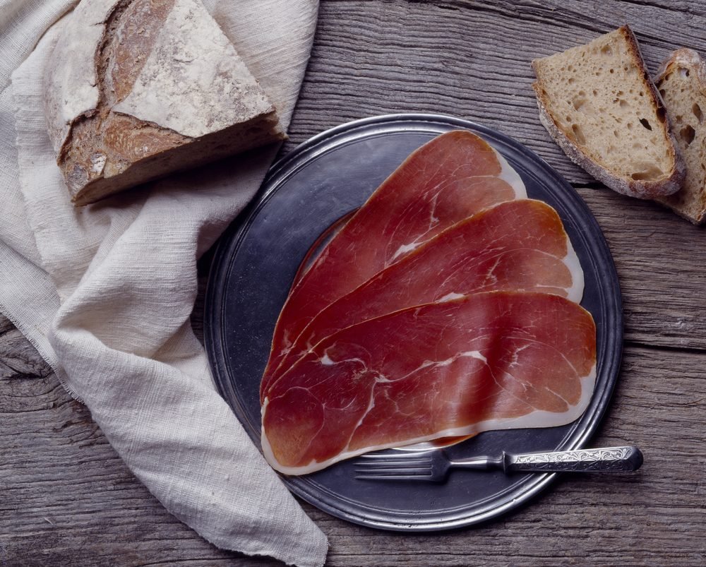 Lâminas de Jambon de Bayonne dispostas em prato metálico com pão rústico ao fundo, típico presunto francês.
