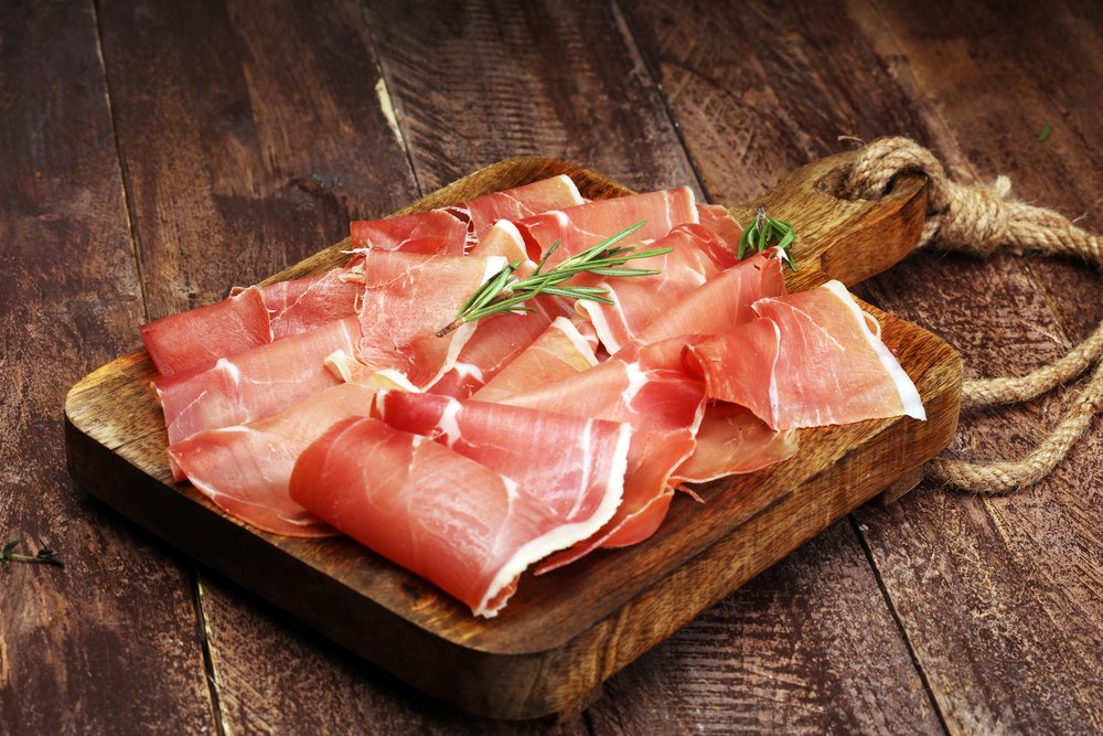 Fatias finas de Prosciutto di Parma sobre tábua de madeira com alecrim, exemplo clássico de presunto cru italiano.