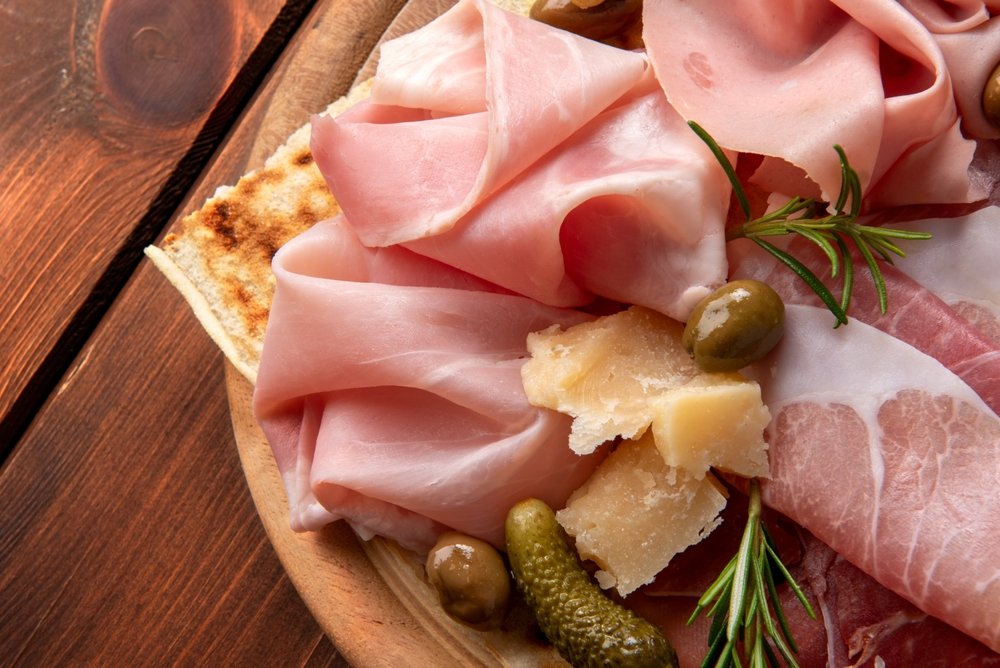 Presunto Royal fatiado em tábua de madeira com azeitonas, pão tostado e alecrim fresco.