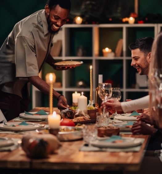 Anfitrião servindo jantar para convidados em mesa decorada com velas para celebração de fim de ano, demonstrando como receber bem em festas memoráveis.