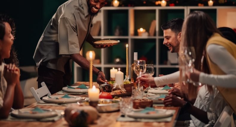 Anfitrião servindo jantar para convidados em mesa decorada com velas para celebração de fim de ano, demonstrando como receber bem em festas memoráveis.