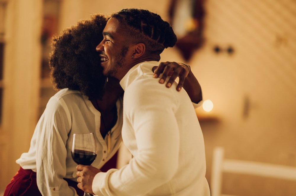 Casal de convidados se abraçando com taças de vinho em jantar de fim de ano, demonstrando cortesia e boas práticas de etiqueta em celebrações.