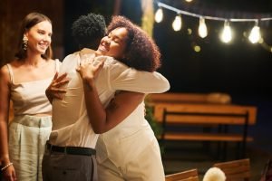 Mulher abraçando amigo afetuosamente em festa de fim de ano com luzes decorativas, mostrando recepção calorosa e hospitalidade do anfitrião.