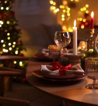 Ceia de Natal simples e prática, mesa posta com velas, taças e árvore iluminada ao fundo para impressionar os convidados