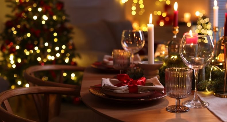 Ceia de Natal simples e prática, mesa posta com velas, taças e árvore iluminada ao fundo para impressionar os convidados