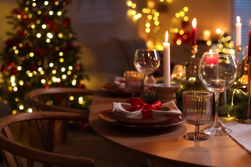 Ceia de Natal simples e prática, mesa posta com velas, taças e árvore iluminada ao fundo para impressionar os convidados