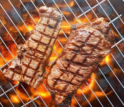 Vista aérea de churrasqueira redonda com picanha e contrafilé grelhando sobre chamas alaranjadas