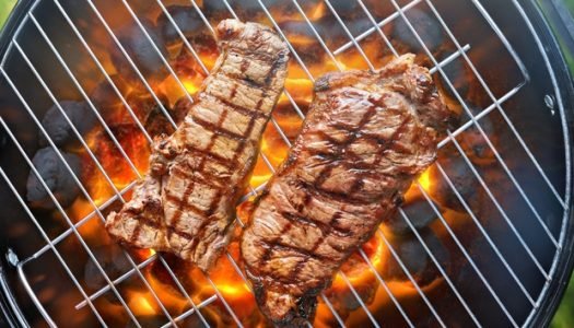 Vista aérea de churrasqueira redonda com picanha e contrafilé grelhando sobre chamas alaranjadas