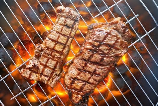 Vista aérea de churrasqueira redonda com picanha e contrafilé grelhando sobre chamas alaranjadas
