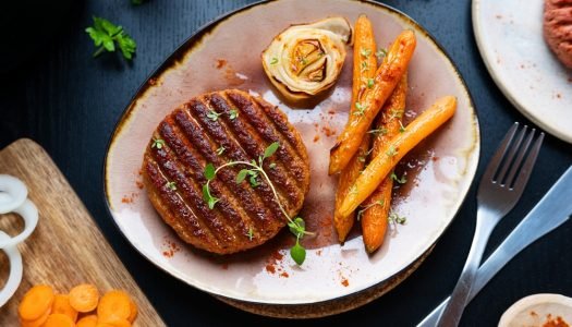Hambúrguer vegetariano caseiro grelhado servido com cenouras assadas e flor de cebola em prato rústico sobre mesa escura