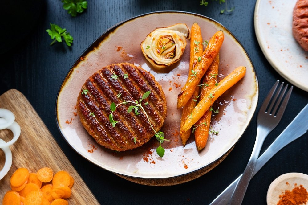 Hambúrguer vegetariano caseiro grelhado servido com cenouras assadas e flor de cebola em prato rústico sobre mesa escura