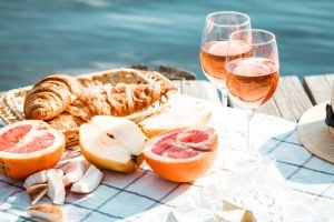 Harmonização de vinho rosé com frutas cítricas e croissants à beira-mar, exemplificando combinações leves e refrescantes para o verão.