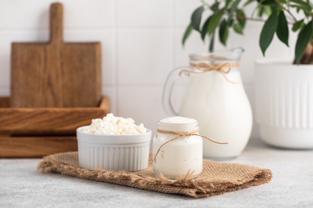 Grãos de kefir de leite em potinho de cerâmica ao lado de jarra com kefir cremoso, representando probiótico natural para saúde intestinal e bem-estar