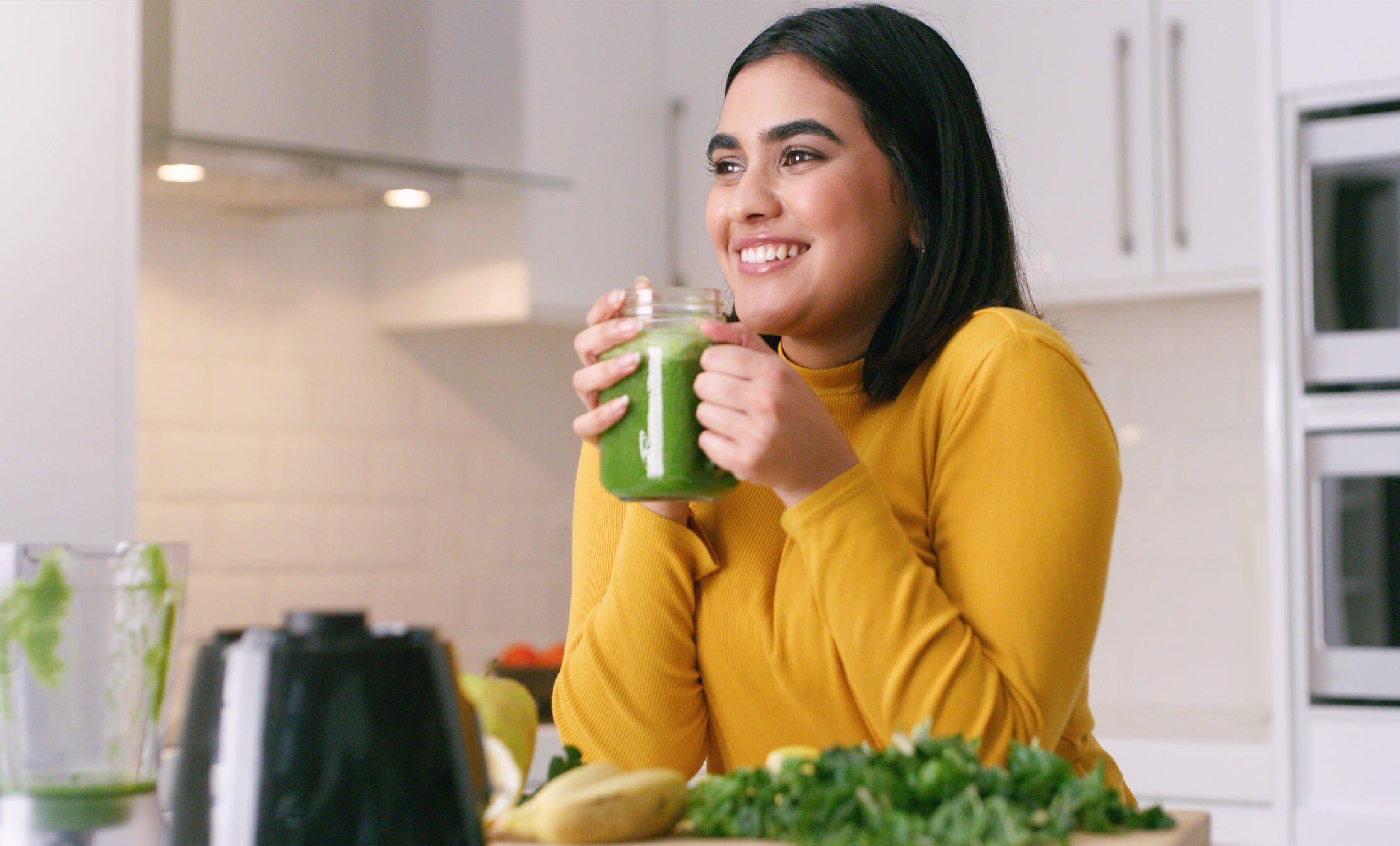 Mulher sorrindo e segurando um copo de suco verde detox.