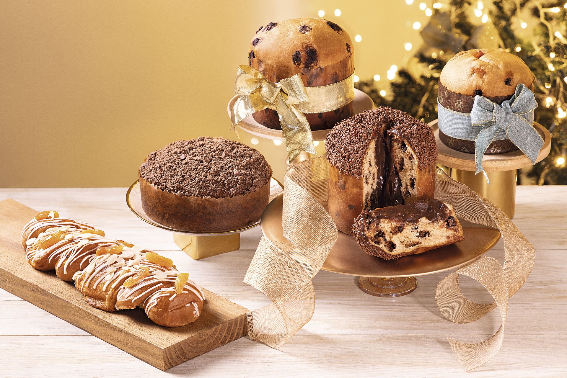 Panetones do Pão para ceias de fim de ano, variedade de panetones recheados e decorados em mesa natalina com luzes ao fundo