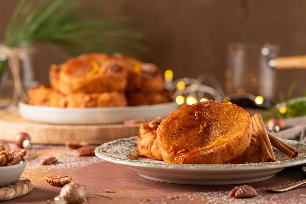 rabanada de natal simples e deliciosa servida em prato branco, com canela em pau e mesa decorada para a ceia de natal