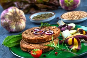 Hambúrguer vegetariano de proteína de soja em prato verde com legumes coloridos, grãos e ervas frescas