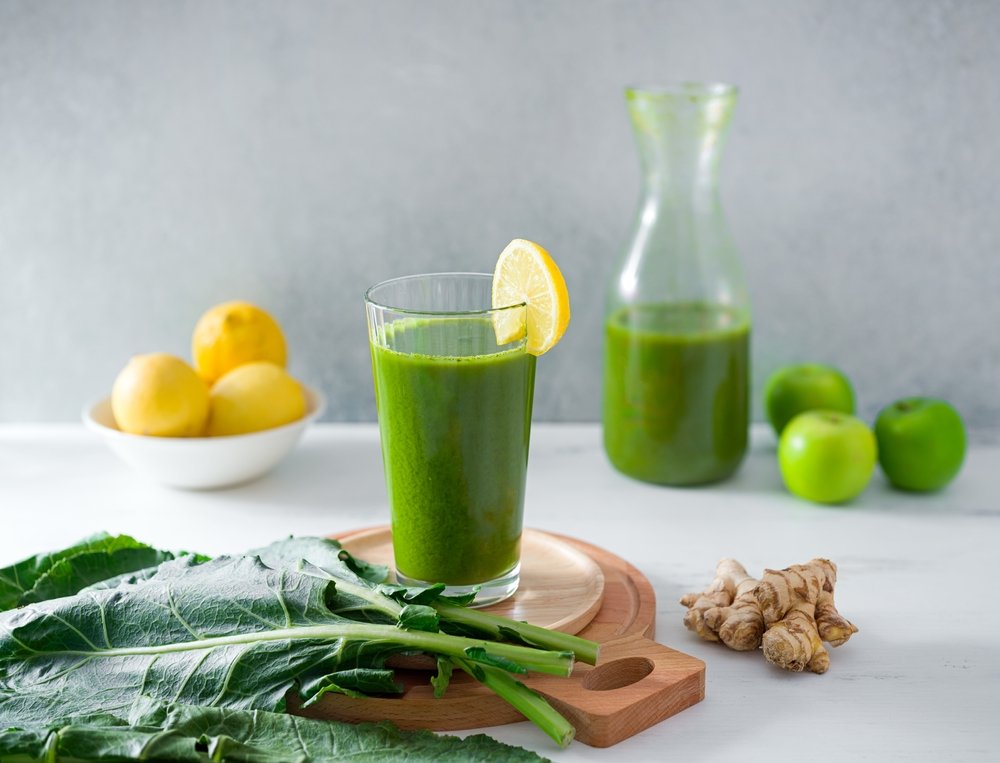 Suco verde detox em copo de vidro com ingredientes frescos como limão couve gengibre e maçã verde sobre mesa clara