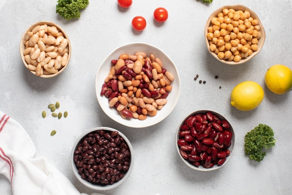 Vários tipos de feijão em tigelas sobre a mesa, como feijão-carioca, feijão-preto, feijão-branco e grão-de-bico, ilustrando os 11 grãos mais consumidos