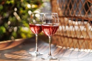 Duas taças de vinho rosé gelado sobre mesa ao ar livre, iluminadas pelo sol, representando vinhos leves e refrescantes para o verão.