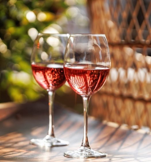 Duas taças de vinho rosé gelado sobre mesa ao ar livre, iluminadas pelo sol, representando vinhos leves e refrescantes para o verão.