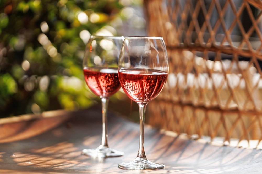 Duas taças de vinho rosé gelado sobre mesa ao ar livre, iluminadas pelo sol, representando vinhos leves e refrescantes para o verão.
