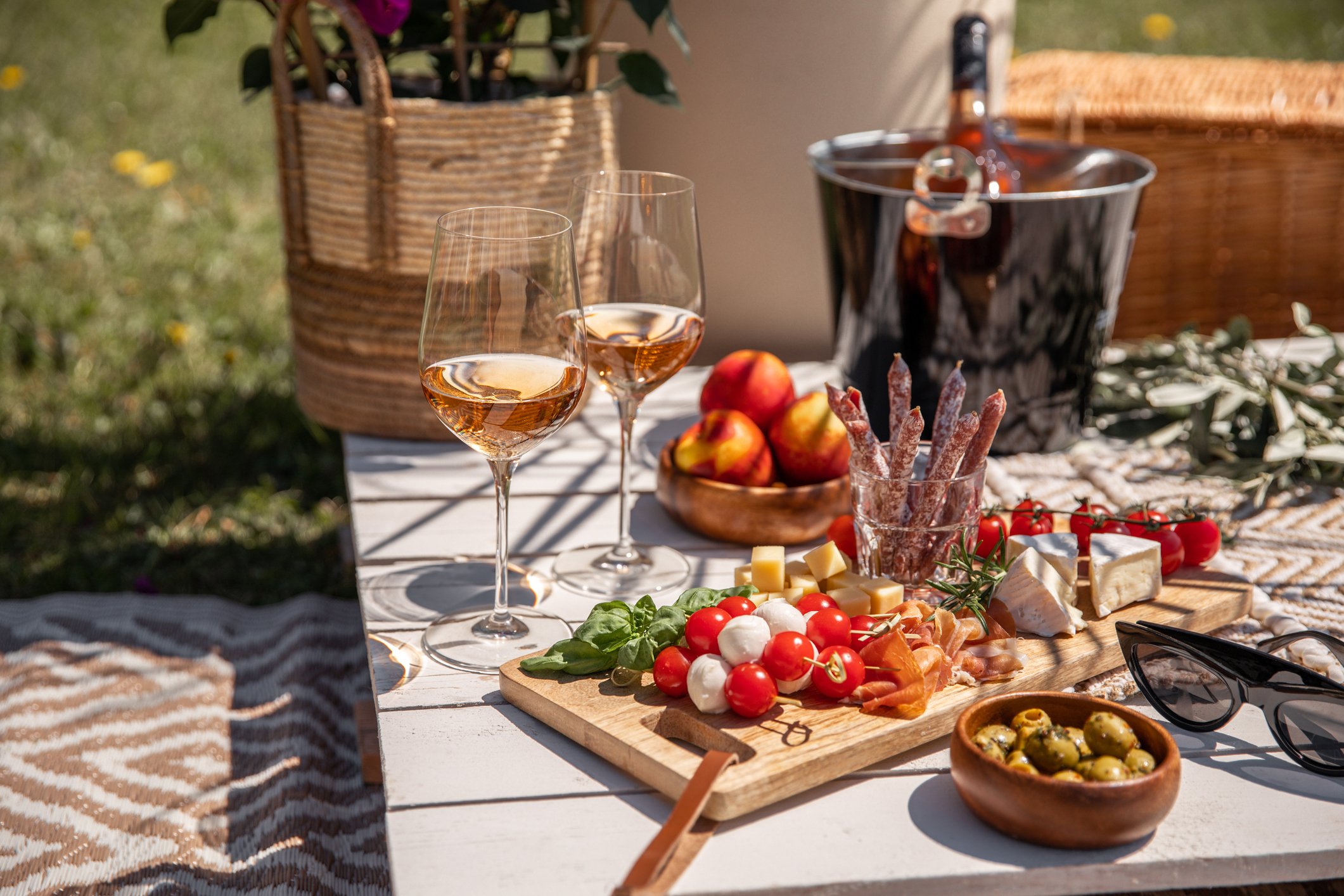 Taças de vinho rosé gelado em piquenique de verão com tábua de queijos e petiscos, balde de gelo e acessórios para servir vinhos leves e refrescantes.