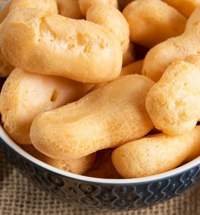 Close de um bowl de cerâmica azul com detalhes em relevo, cheio de biscoitos de polvilho doce em formato alongado e cilíndrico.