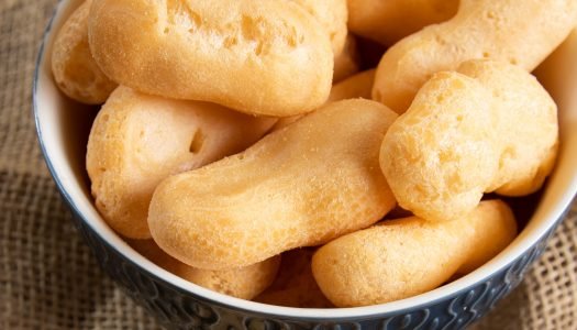 Close de um bowl de cerâmica azul com detalhes em relevo, cheio de biscoitos de polvilho doce em formato alongado e cilíndrico.