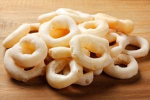 Pilha de biscoitos de polvilho doce assados em formato circular de rosquinha, dispostos sobre uma superfície de madeira clara.